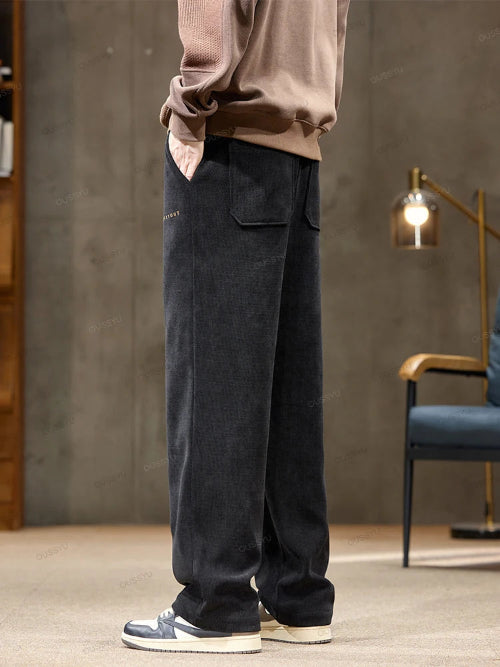 Person wearing dark pants and a beige sweater in a room with a lamp and chair.