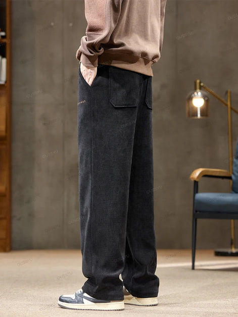 Person wearing dark pants and a beige sweater in a room with a lamp and chair.