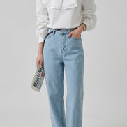 A woman wearing a white long-sleeve blouse with a dramatic oversized ruffled collar and light-wash blue jeans, 