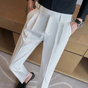 A person wearing high-waisted off-white trousers with a matching belt, paired with a black shirt and black loafers, standing in front of a wooden desk.