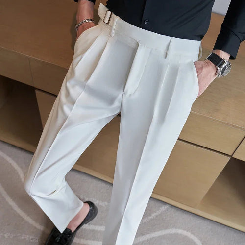 A person wearing high-waisted off-white trousers with a matching belt, paired with a black shirt and black loafers, standing in front of a wooden desk.