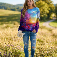 A woman wearing a long-sleeve crewneck sweatshirt with a vibrant, multicolored abstract landscape print featuring a tree, sunset, and sky. 