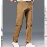 A person wearing tan straight-leg pants with white sneakers, shown from the waist down against a gray studio background.