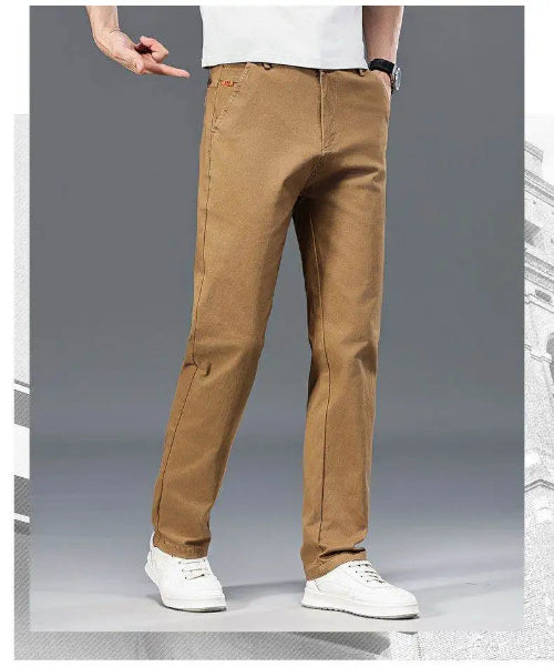 A person wearing tan straight-leg pants with white sneakers, shown from the waist down against a gray studio background.