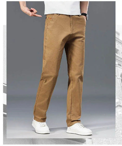 A person wearing tan straight-leg pants with white sneakers, shown from the waist down against a gray studio background.