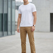 A person wearing tan straight-leg pants with white sneakers, shown from the waist down against a gray studio background.