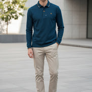 Blue polo shirt with a brand logo held by a hand, with hangers in the background.