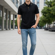 Black polo shirt with a brand logo held by a hand in a clothing store.