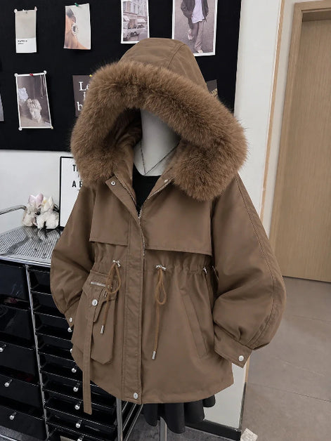 A brown hooded parka jacket with a large fluffy faux-fur trimmed hood, displayed on a mannequin in an indoor boutique setting.