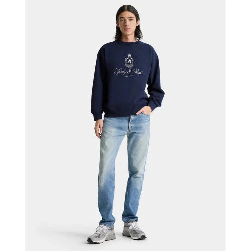 Person wearing a navy blue sweatshirt with a logo and light blue jeans on a white background