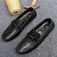 Black leather loafers on a gray surface with a spool of thread and wooden mallet.