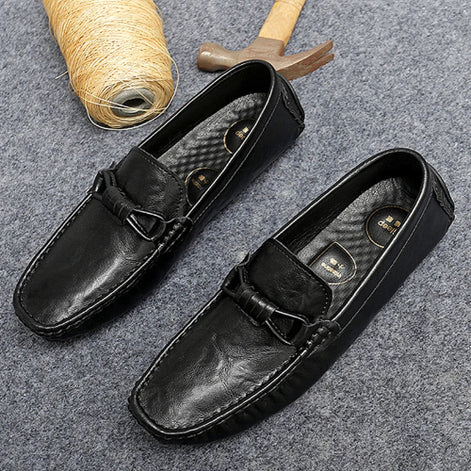 Black leather loafers on a gray surface with a spool of thread and wooden mallet.