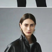 Close-up of a woman wearing a black faux leather jacket with a raised collar over a white top against a gray background⠋