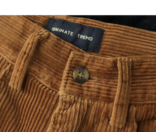 Close-up of brown corduroy trousers showing the waistband, belt loops, button, and a black label that reads OMINATE TREND.