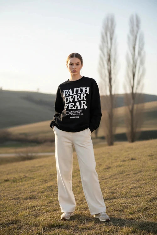 Black sweatshirt with 'Faith Over Fear' text on a wooden background