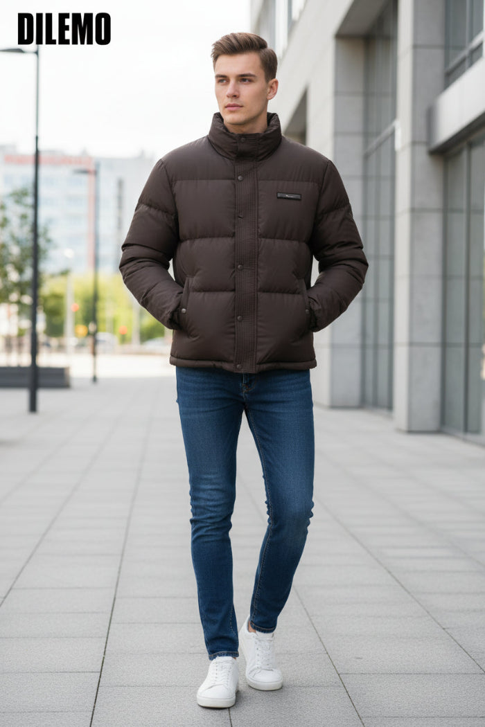 A dark brown puffer jacket with a high collar and snap-button front, shown on a hanger with a hand holding the lower right side. Three feature callout graphics on the left mention 85% down, thick warm lining, and fluffy soft texture.