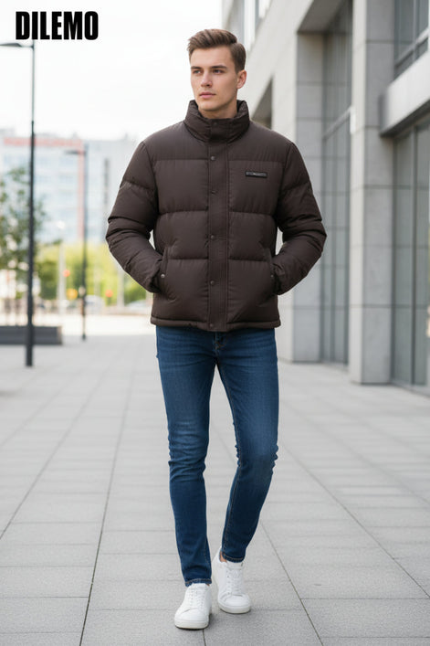 A dark brown puffer jacket with a high collar and snap-button front, shown on a hanger with a hand holding the lower right side. Three feature callout graphics on the left mention 85% down, thick warm lining, and fluffy soft texture.