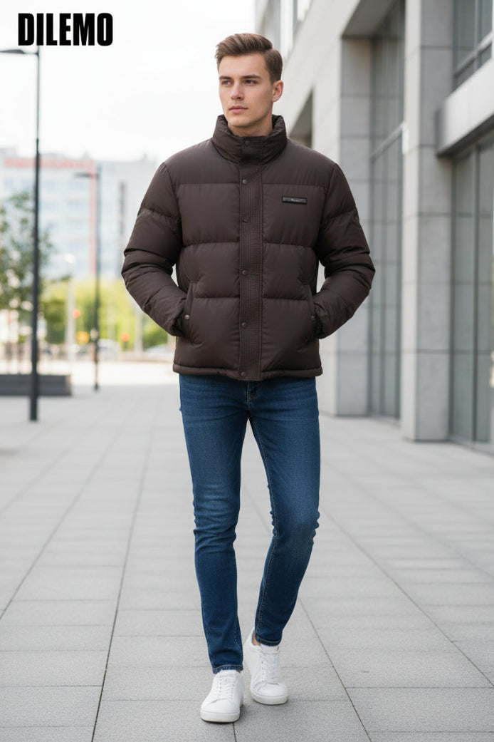 A dark brown puffer jacket with a high collar and snap-button front, shown on a hanger with a hand holding the lower right side. Three feature callout graphics on the left mention 85% down, thick warm lining, and fluffy soft texture.