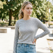 A woman wearing a fitted light gray long-sleeve turtleneck sweater and light blue jeans, shown in a mirror selfie against a beige tiled wall.