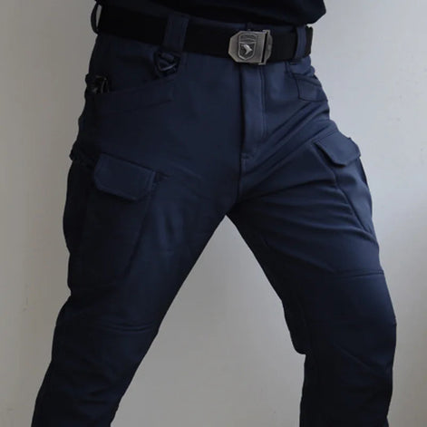 Front view of a model wearing navy blue cargo pants with flap thigh pockets and a black buckle belt against a light gray background.⠋