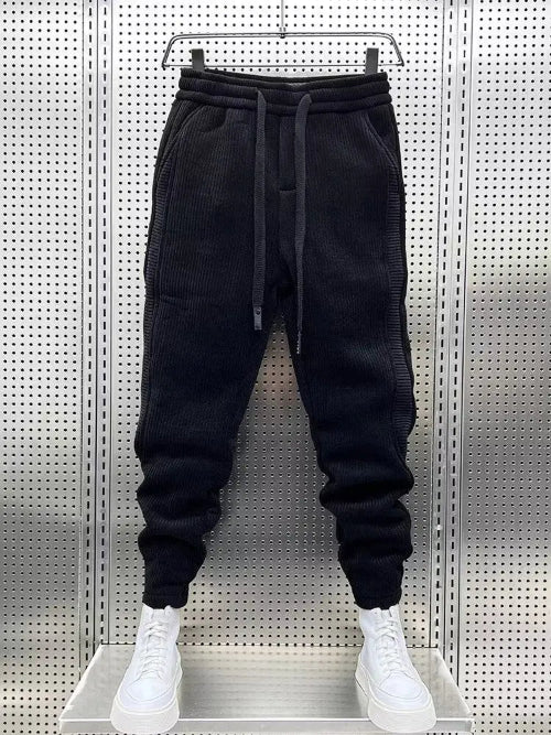 Black baggy sweatpants hanging on a hanger with white sneakers below.