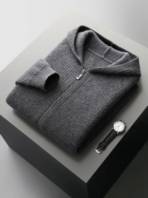 A folded dark gray ribbed zip-up sweater with a hood, displayed on a dark gray pedestal next to a black leather strap watch.