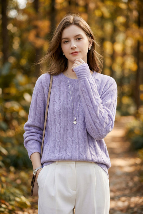 A person wearing a light lavender cable-knit sweater and white pants, holding a dark green phone to take a mirror selfie against a plain white background.