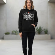 A black pullover hoodie laid flat with a festive white graphic reading 'family Christmas 2026' and a small Santa hat accent, 