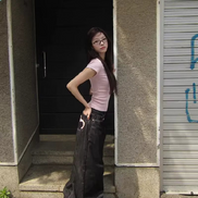 Side view of a woman wearing dark-wash loose-fit jeans with a pink heart outline on a back pocket, standing outside by steps.
