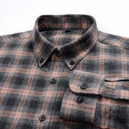 A close-up of a long-sleeve plaid button-down shirt in charcoal gray and dusty rose pink, featuring a classic collar, dark buttons, and a chest pocket.