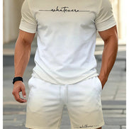A man wearing a matching beige/cream two-piece lounge set consisting of a short-sleeve crewneck t-shirt and shorts, both featuring the word 'whatevers' printed in black script 