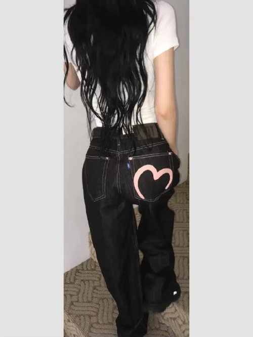 Rear view of a woman wearing dark-wash loose-fit jeans with contrast stitching and a pink heart outline on the right back pocket.