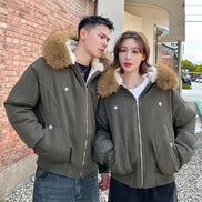 Two people wearing matching green jackets with fur-lined hoods standing outdoors.