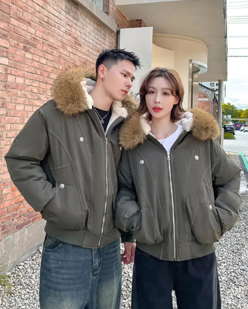 Two people wearing matching green jackets with fur-lined hoods standing outdoors.