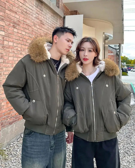 Two people wearing matching green jackets with fur-lined hoods standing outdoors.