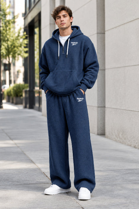 A man wearing a navy blue Reebok waffle-knit lounge set, featuring a pullover hoodie with a half-zip front and matching sweatpants,