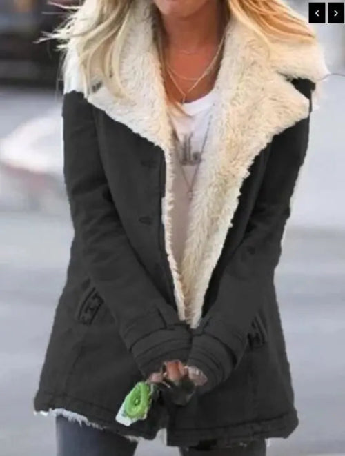 Woman outdoors wearing a black coat with wide cream fleece-look lapels, front pockets and cuff tabs over a white top