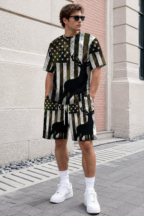 A person wearing a matching short-sleeve t-shirt and shorts set with an American flag and deer silhouette print, standing outdoors against a stone wall.