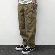 Model wearing khaki loose-fit cargo pants with large flap thigh pockets and stitched knee panels, paired with black sneakers.