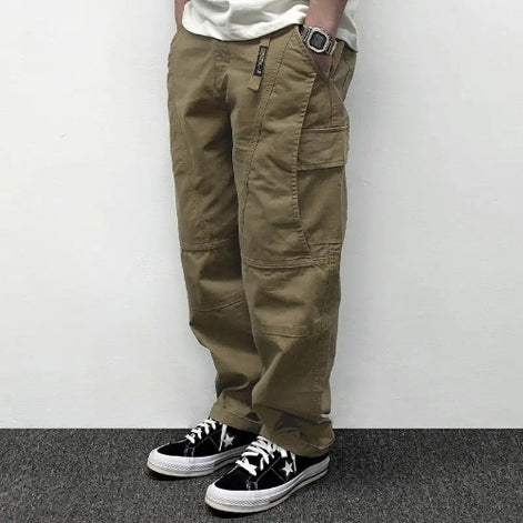 Model wearing khaki loose-fit cargo pants with large flap thigh pockets and stitched knee panels, paired with black sneakers.