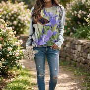 A woman wearing a light gray sweatshirt with a large watercolor-style print of purple irises and a butterfly, paired with blue jeans. 