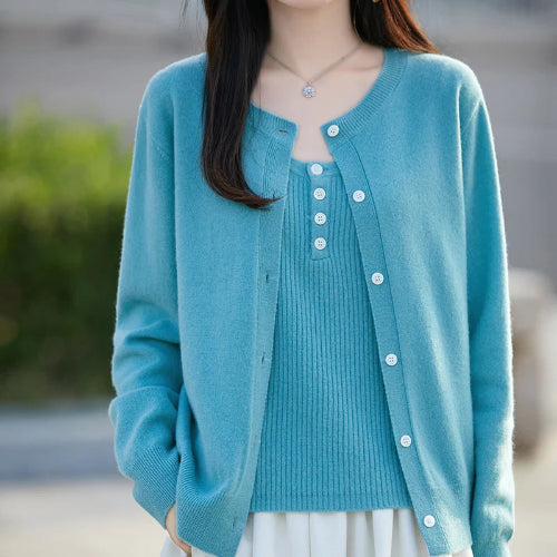 A woman wearing a light blue knit cardigan over a matching ribbed top, shown from the shoulders to the hips against a softly blurred outdoor background.