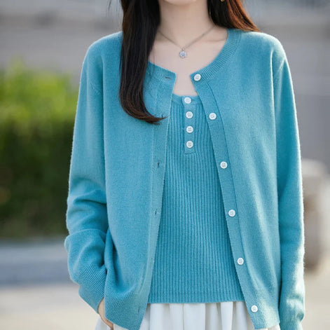 A woman wearing a light blue knit cardigan over a matching ribbed top, shown from the shoulders to the hips against a softly blurred outdoor background.
