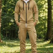 A man wearing a matching tan zip-up hoodie and jogger pants set with white sneakers,