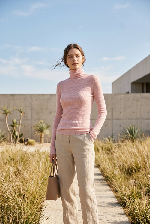 A person wearing a fitted long-sleeve pink ribbed turtleneck sweater, paired with a brown textured skirt, photographed indoors against a light gray tiled wall.