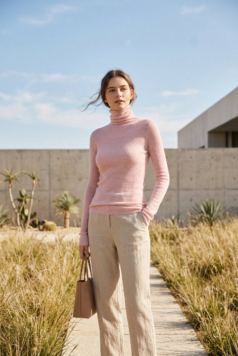 A person wearing a fitted long-sleeve pink ribbed turtleneck sweater, paired with a brown textured skirt, photographed indoors against a light gray tiled wall.
