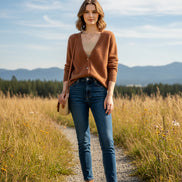 A person wearing a fuzzy brown cardigan over a beige ribbed top, standing indoors near large windows with a city view.