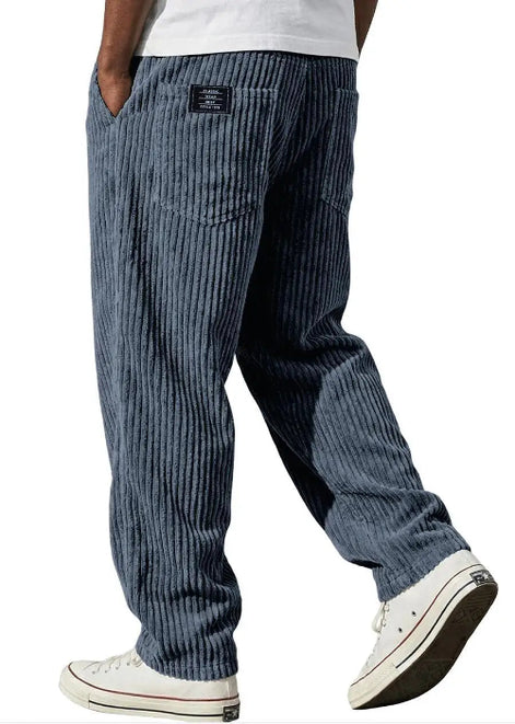 A person wearing blue vertically striped corduroy pants, shown from the waist down, paired with a white t-shirt and white low-top sneakers.