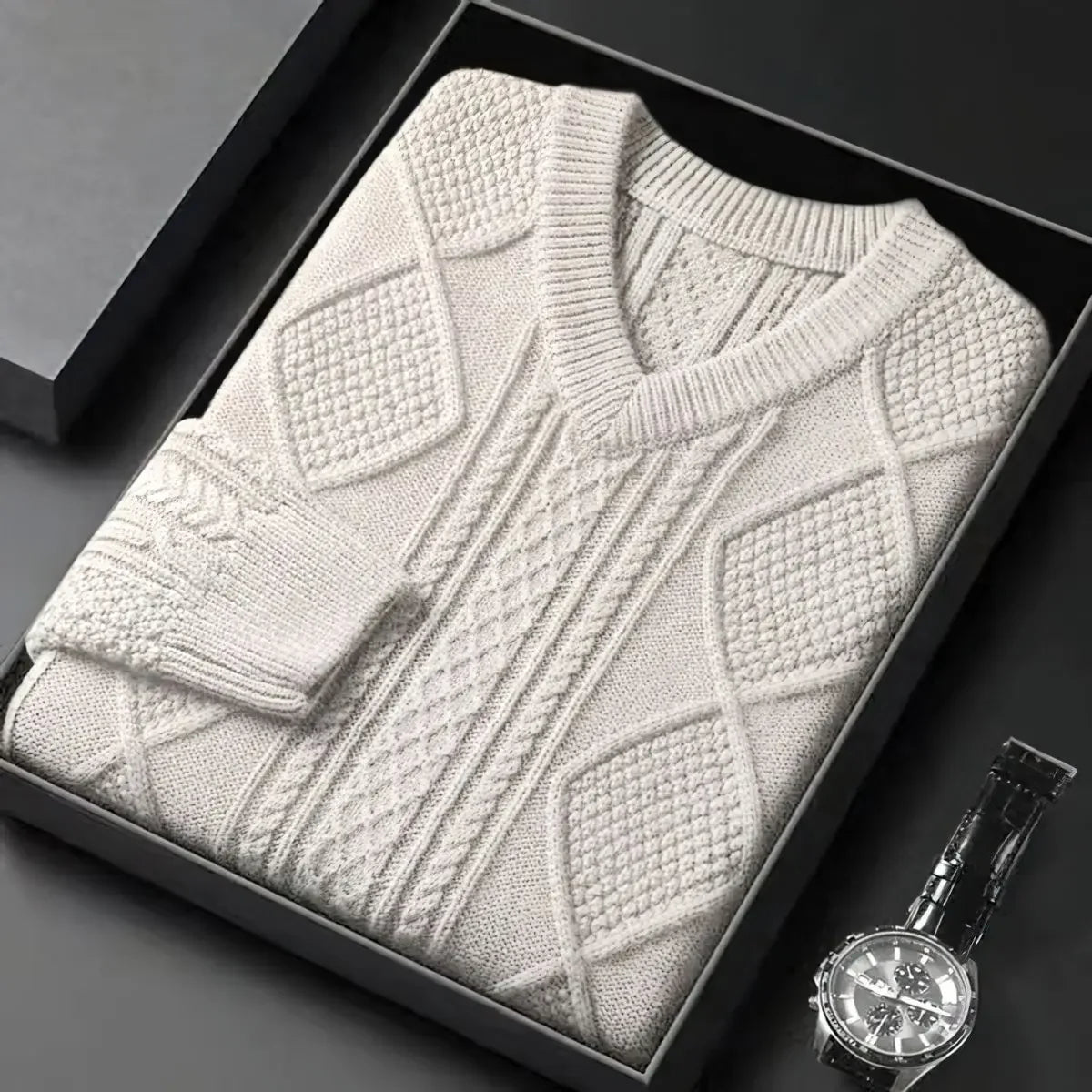Folded white sweater in a black box with a watch on a dark surface