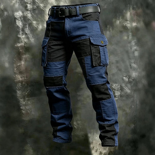 Navy blue and black color-block cargo pants with flap thigh pockets and a black belt against a textured gray background.